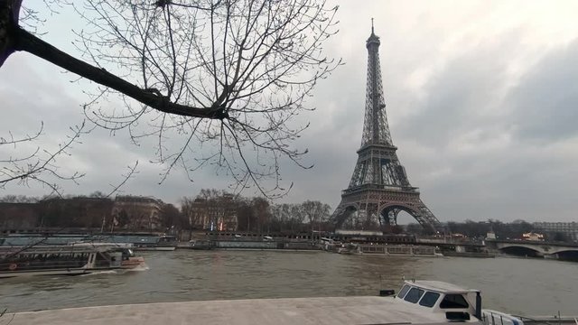 4K, Eiffel Tower and Seine river with boat in back of tree branches of a winter day Paris, France. Trees and cloudy sky in famous touristic places Europe. Rainy day with the tour Eiffel background-Dan