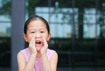 Portrait little Asian child girl acting and shouting through hands like megaphone. Communication concept.