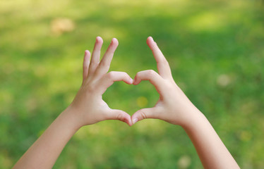 Child hands with heart sign on blur green lawn background.