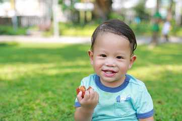 Happy Asian baby boy enjoy eating fried chicken in the green garden outdoor.