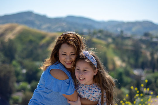 Latina Mother And Daughter Smiling And Laughing On A Hill In Front Of Yellow Flowers