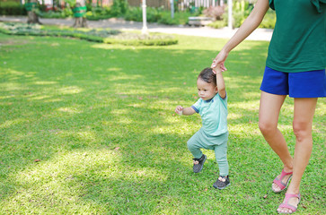 Asian mother learning her infant baby to walk first steps on the green grass garden.