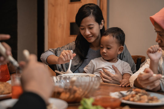 Asian Mother With Her Son Eating Together While Dinner. Mom Feeding Her Toddler Son