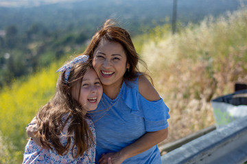 Latina Mother and Daughter Smiling and laughing on a hill in front of yellow flowers