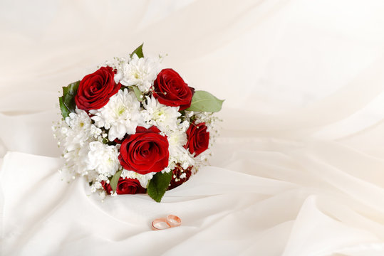 wedding concept bouquet of red roses and wedding gold rings on light pastel background. copy space