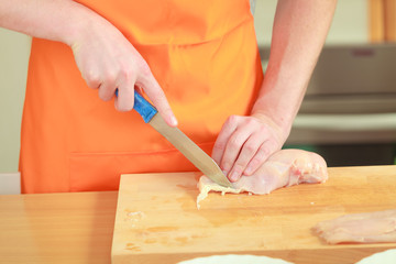 Man cutting raw chicken meat on wooden board