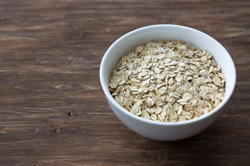 Oat flakes, rolled oatmeal in a white bowl on a wooden table