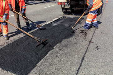 The working team evenly distributes part of the asphalt with shovels during road construction.
