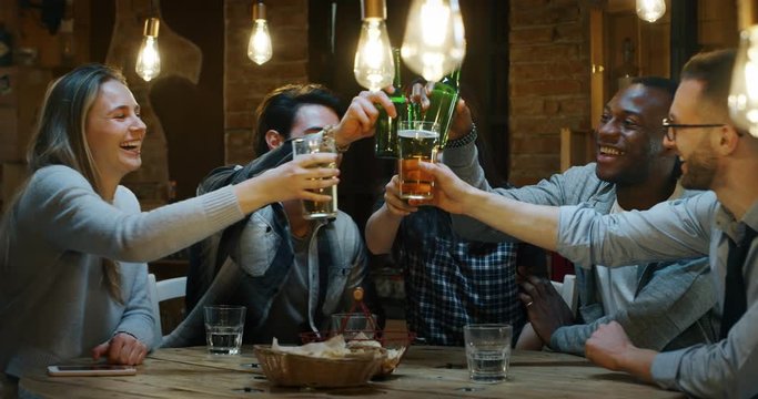 Slow motion of happy young friends having fun together drinking beer and clinking glasses in a pub. 
