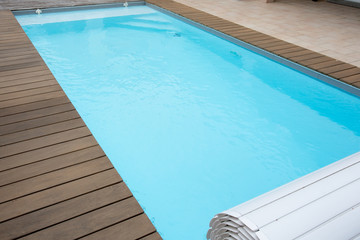 blue swimming pool with teak wood flooring in home garden summer