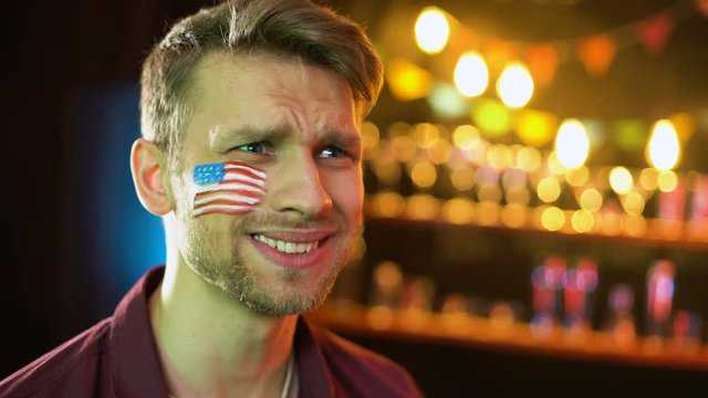 Nervous american soccer fan with flag on cheek unhappy with game result