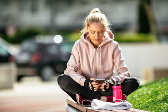 Sporty girl on the phone. Girl uses her phone after a workout. Woman takes a break from training uses phone. Sport.