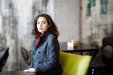 Young attractive girl sitting in a cafe, dressed in warm coat. Cozy atmosphere.
