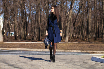 Portrait of a young beautiful woman in blue coat with a bag walking in spring park