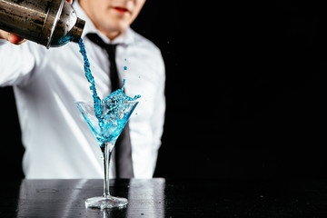 Barman makes blue martini. Barkeeper shakes and makes a martini cocktail. Cocktail on a black...