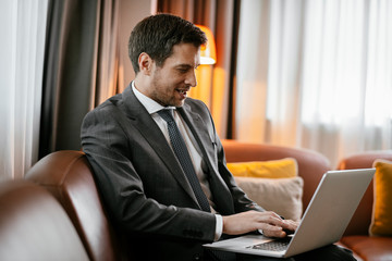 Man working on his laptop at the hotel. Executive manager typing on his laptop. Businessman sitting on the sofa working.