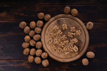 Fototapeta na wymiar Cracked and whole walnuts lying on round wooden plate and wooden table, top view. Healthy nuts and seeds composition.