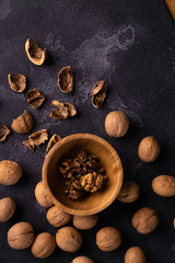 Obraz na płótnie Canvas Cracked walnuts in wooden bowl and on black slate surface. Healthy nuts and seeds composition.
