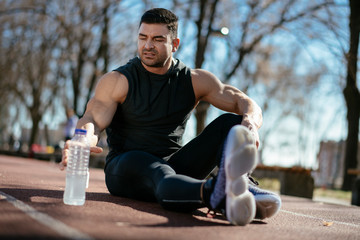Thirsty athlete. Man reaching for a bottle of water. Guy trains outdoors.
