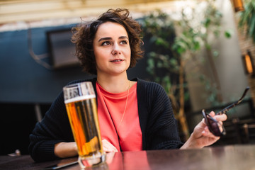 Girl having a beer while waiting for a friend. Short haired woman drinking beer at a bar.  Brunette drinks beer.