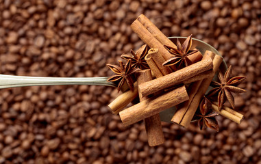 Spoon with anise and cinnamon sticks on the background of coffee beans.