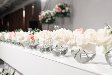 Small flower arrangements in ball glass vases. The table of the newlyweds. Interior of restaurant for wedding dinner, ready for guests. Catering concept.