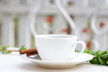 Aromatic coffee in a summer cafe in a white cup with cinnamon sticks. Beautiful green leaves.