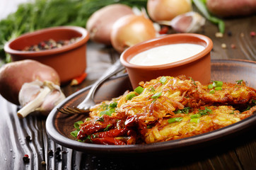 Homemade tasty potato pancakes in clay dish with sun-dried tomatoes and sour cream