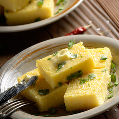 Polenta with butter and greens on clay dish on wooden rustic table