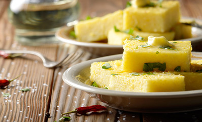 Polenta with butter and greens on clay dish on wooden rustic table