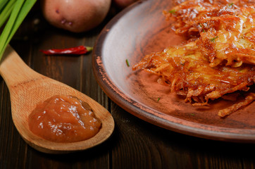 Homemade tasty potato pancakes in clay dish with applesauce