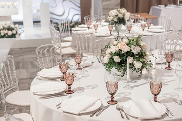 Flower arrangement in the center of the table. Interior of restaurant for wedding dinner, ready for guests. Round Banquet table served. Catering concept.