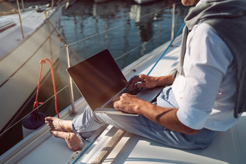 Senior man is working during the vacation on a sailboat - obrazy, fototapety, plakaty