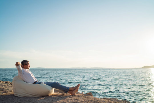 Senior man lying on deck chair on the beach during sunset