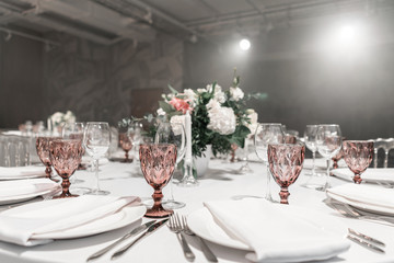 Wine glasses on round Banquet table served. Interior of restaurant for wedding dinner, ready for guests. Decorated with floral arrangement. Dishes, wine glasses and napkins. Catering concept.