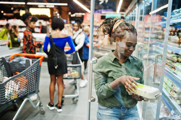 Group of african womans with shopping carts near refrigerator shelf selling dairy products egg carton in the supermarket.