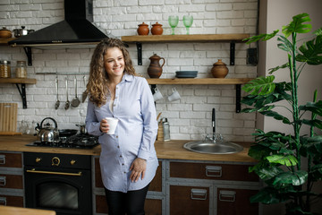 Portrait of a pregnant woman drinking orange juice while watching the house, is in the kitchen.