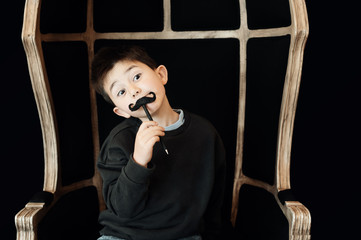 Happy kid posing with a fake moustache on black background