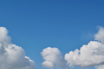Obraz premium On the clear blue sky below the Cumulus fluffy white clouds are arranged in an arc. One cloud in the middle below, two on the sides. Meteorology, weather forecast. Background, backdrop.