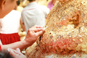 Hand of people are putting gold leaf Buddha sculpture for faith is symbol Buddhism, Religion concept