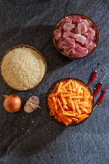 Ingredients for making pilaf, rice, meat, onions and carrots on a dark background