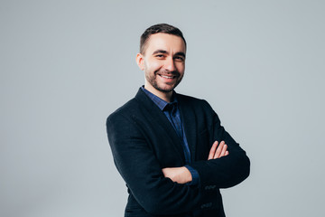 Portrait of attractive young businessman in suit standing with arms crossed on light grey background