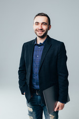 Handsome businessman standing with laptop over gray background.