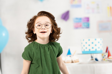 Fototapeta na wymiar adorable kid in glasses looking at camera and smiling during birthday celebration at home