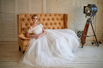 Fototapeta na wymiar A beautiful petite blonde is sitting on the couch. The bride in a lace dress. Bride's morning