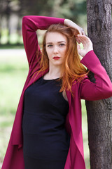 Red-haired girl posing near a tree in red clothes.