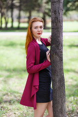 Red-haired girl posing near a tree in red clothes.