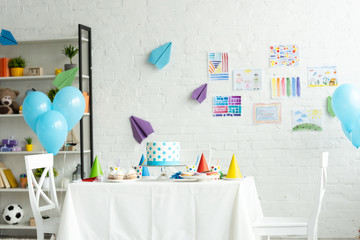 festive cake and party caps on table in room decorated for birthday party with air balloons