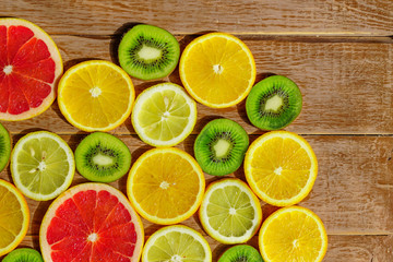 Fototapeta na wymiar frame with slices of oranges, lemons, kiwi, grapefruit pattern on wooden background. Copy space