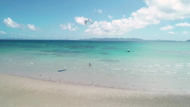 Aerial view of the kiter a large white training kite on the seashore. Extreme sports kitesurfing in tropical blue ocean, clear beach. El Nido, Philippines.